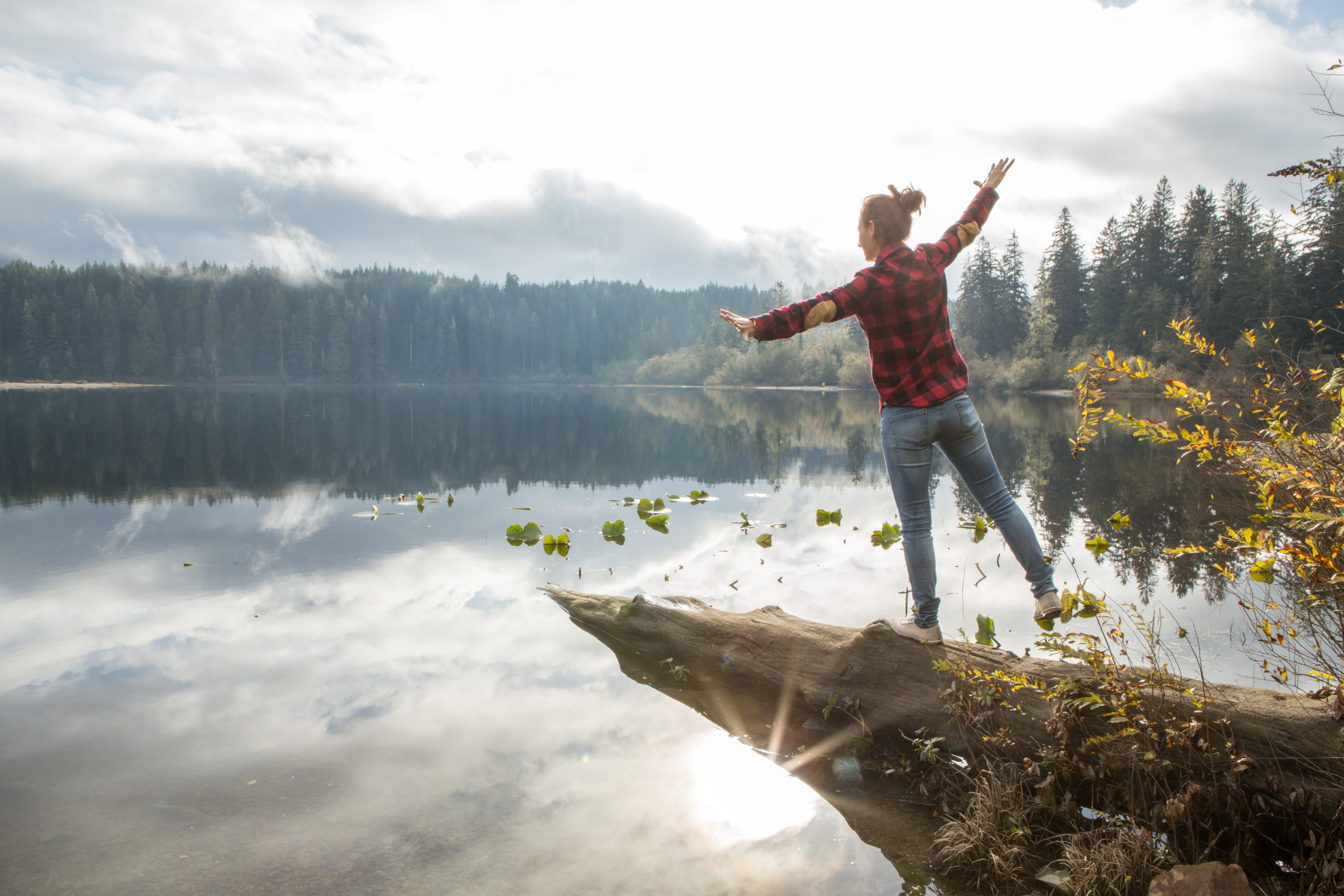 Young woman balances on a tree log above the lake